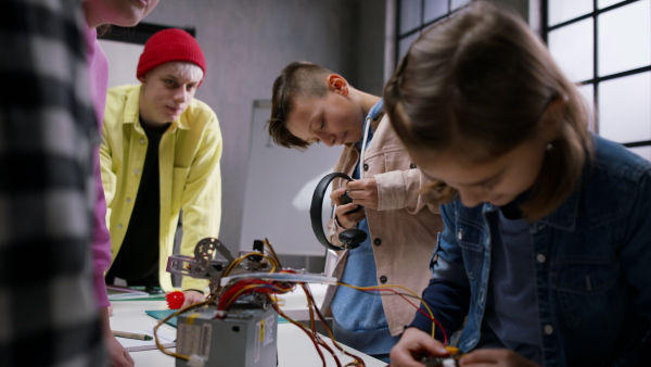 A group of happy kids with their science teacher with electric toys and robots at robotics classroom