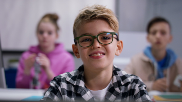 A happy student boy sitting in classroom and looking at camera.