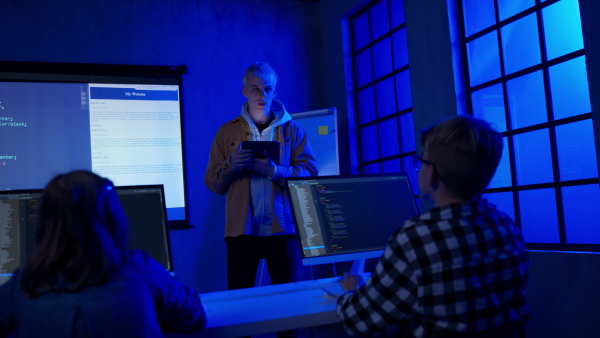 A teacher giving computer science lecture to young students in dark room. Room. Explaining Information Technology.