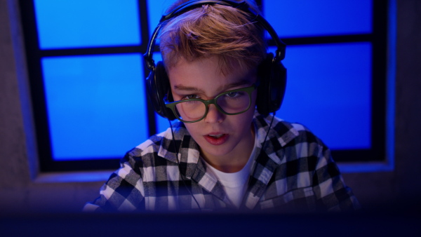 A young gamer boy with headphones playing computer video game.