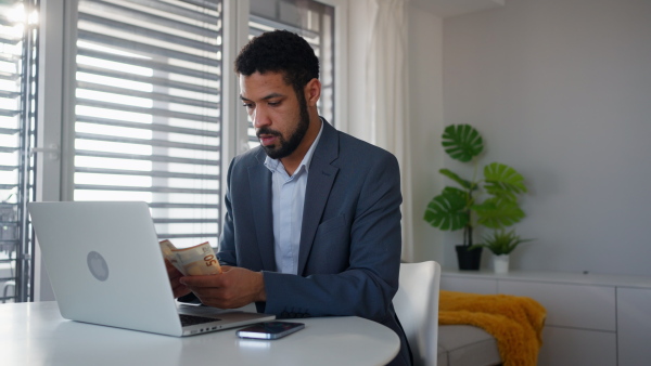 A depressed businessman man counting euro money working on computer at office desk, inflation concept.