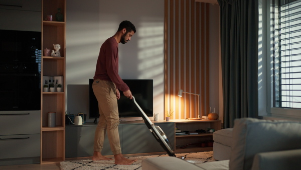 A young man vacuum cleaning carpet in living room