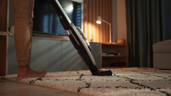 A lowsection of man hoovering carpet with vacuum cleaner in living room