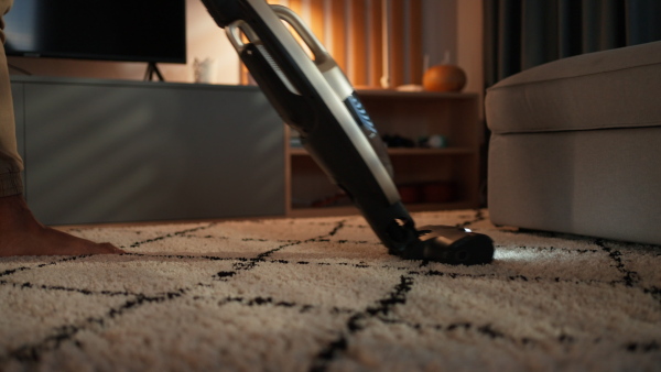 An unrecognizable an vacuum cleaning carpet in living room, lowsection close-up