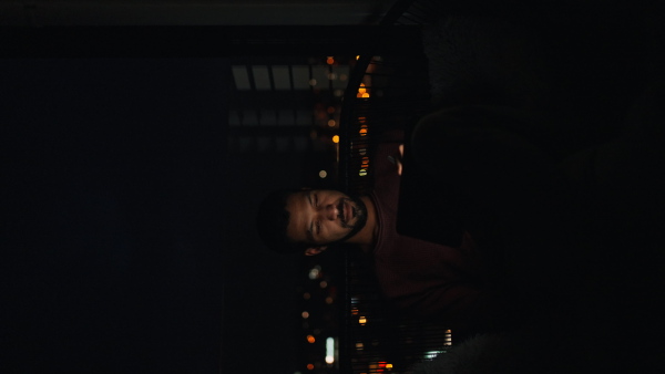 A young African AMerican man sitting on balcony with urban view and using tablet at night