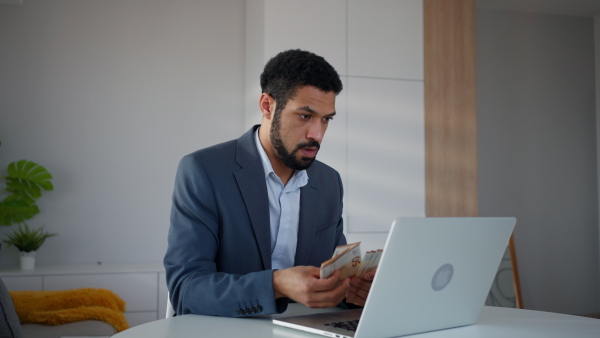 A depressed businessman man counting euro money working on computer at office desk, inflation concept.