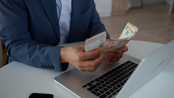 A businessman man with euro money in his hands is working on a computer keyboard at office desk, close-up