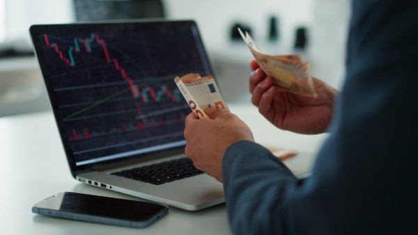 A businessman man counting euro money working on computer at office desk, inflation concept.