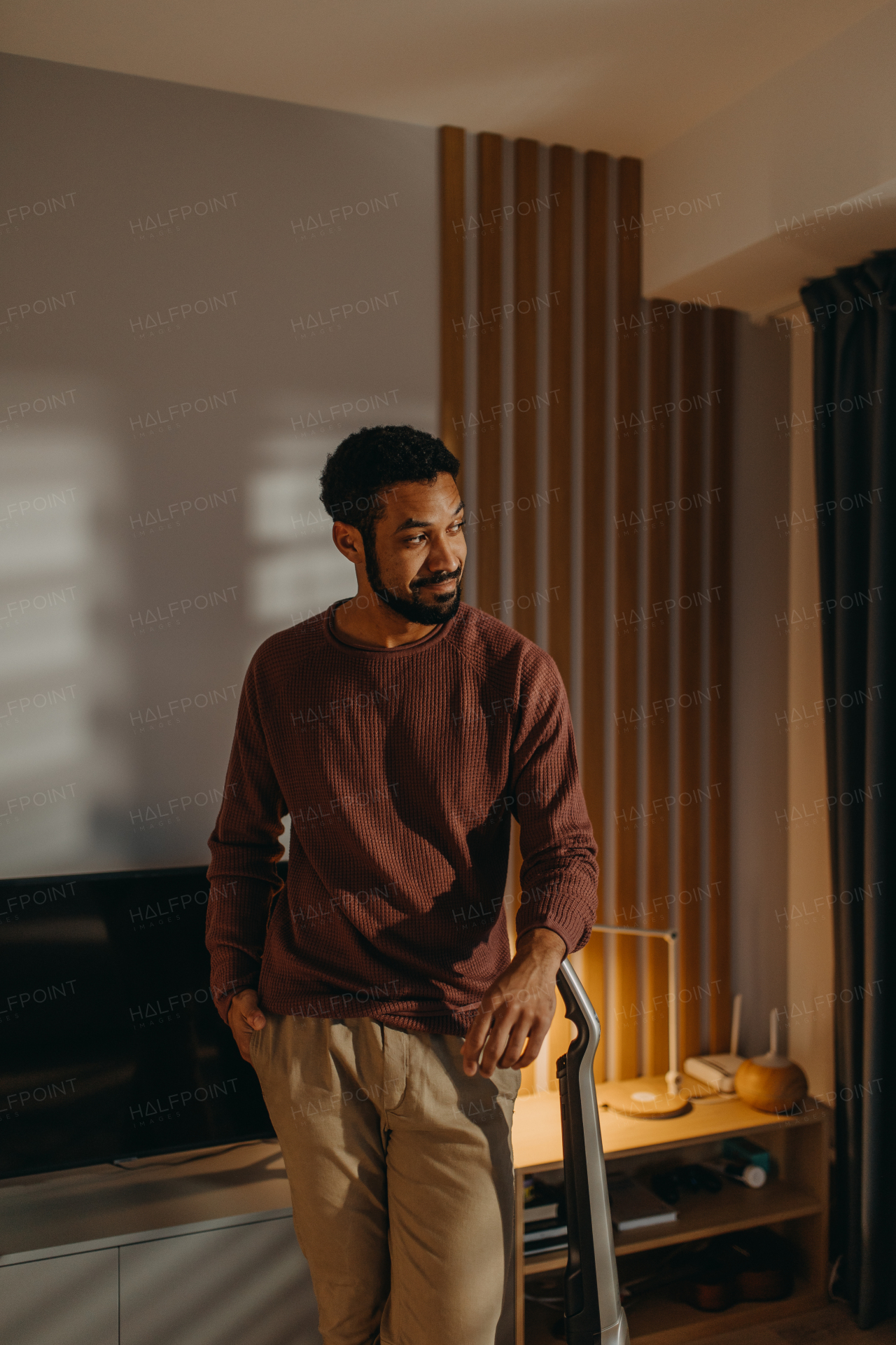 A young man hoovering carpet with vacuum cleaner in living room