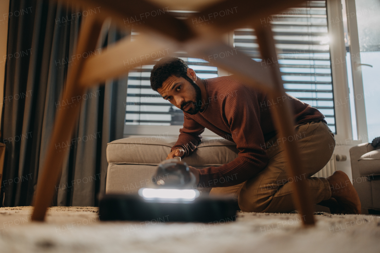 A young man hoovering carpet with vacuum cleaner in living room