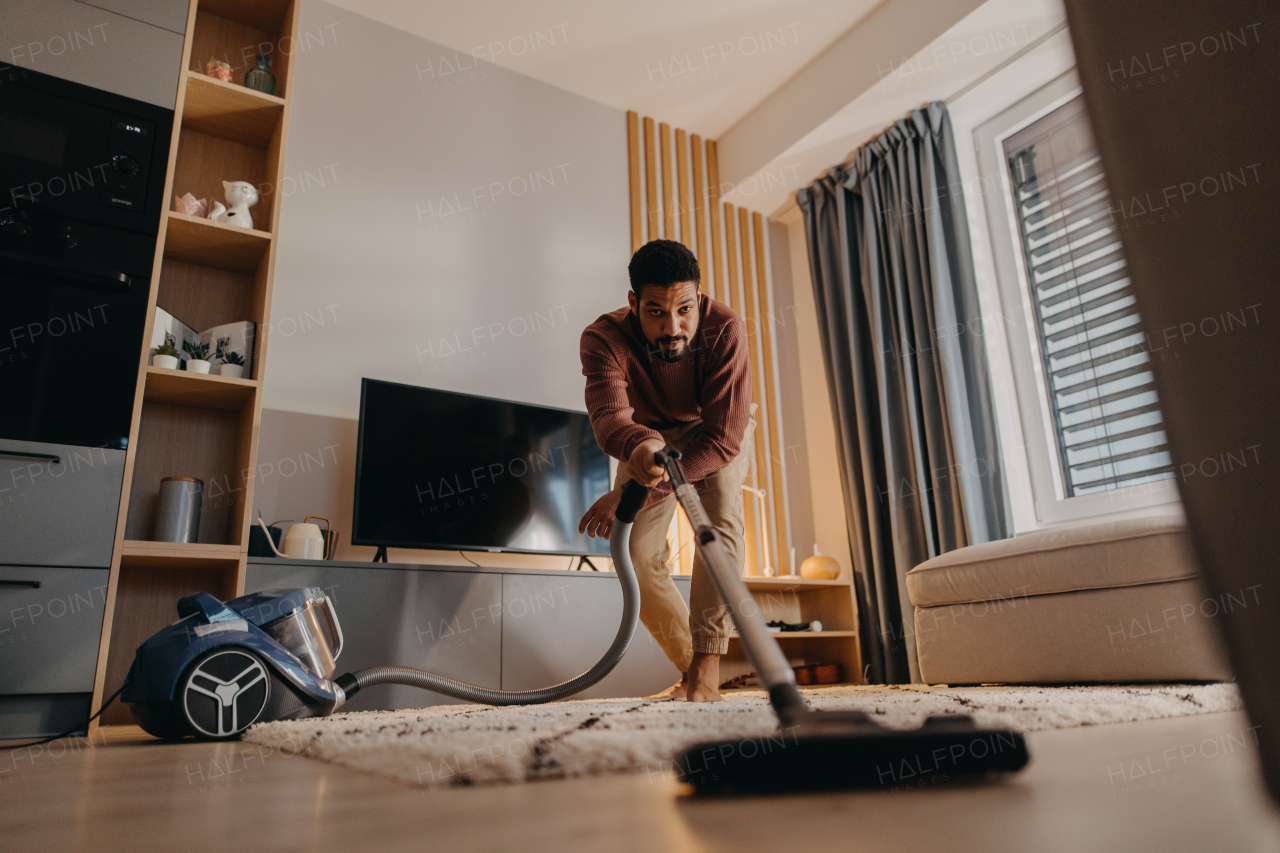 A young man hoovering carpet with vacuum cleaner in living room