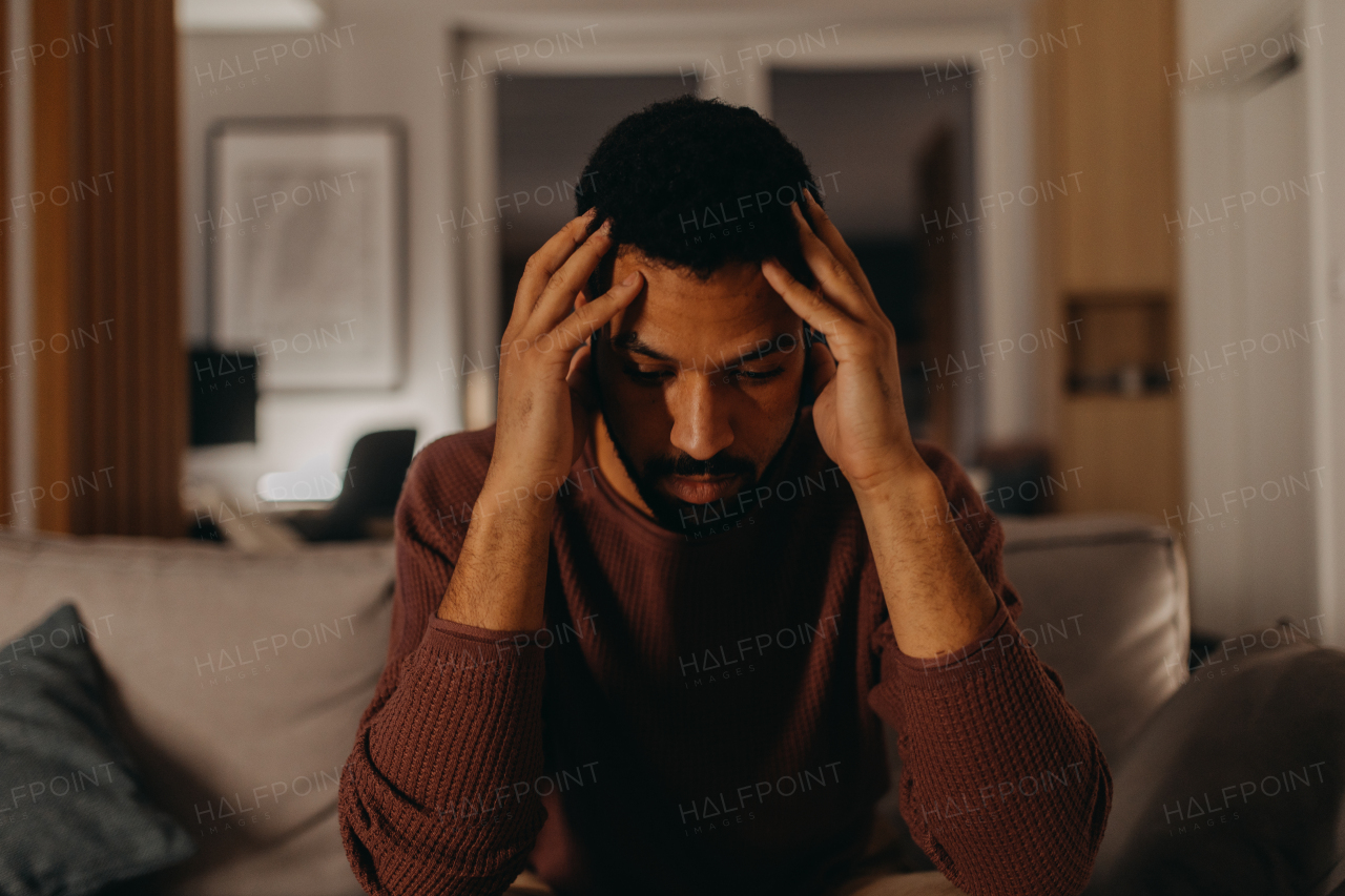 A portrait od depressed young African - American man with head in hands sitting at home.