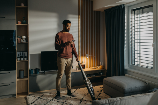 A young man hoovering carpet with vacuum cleaner in living room