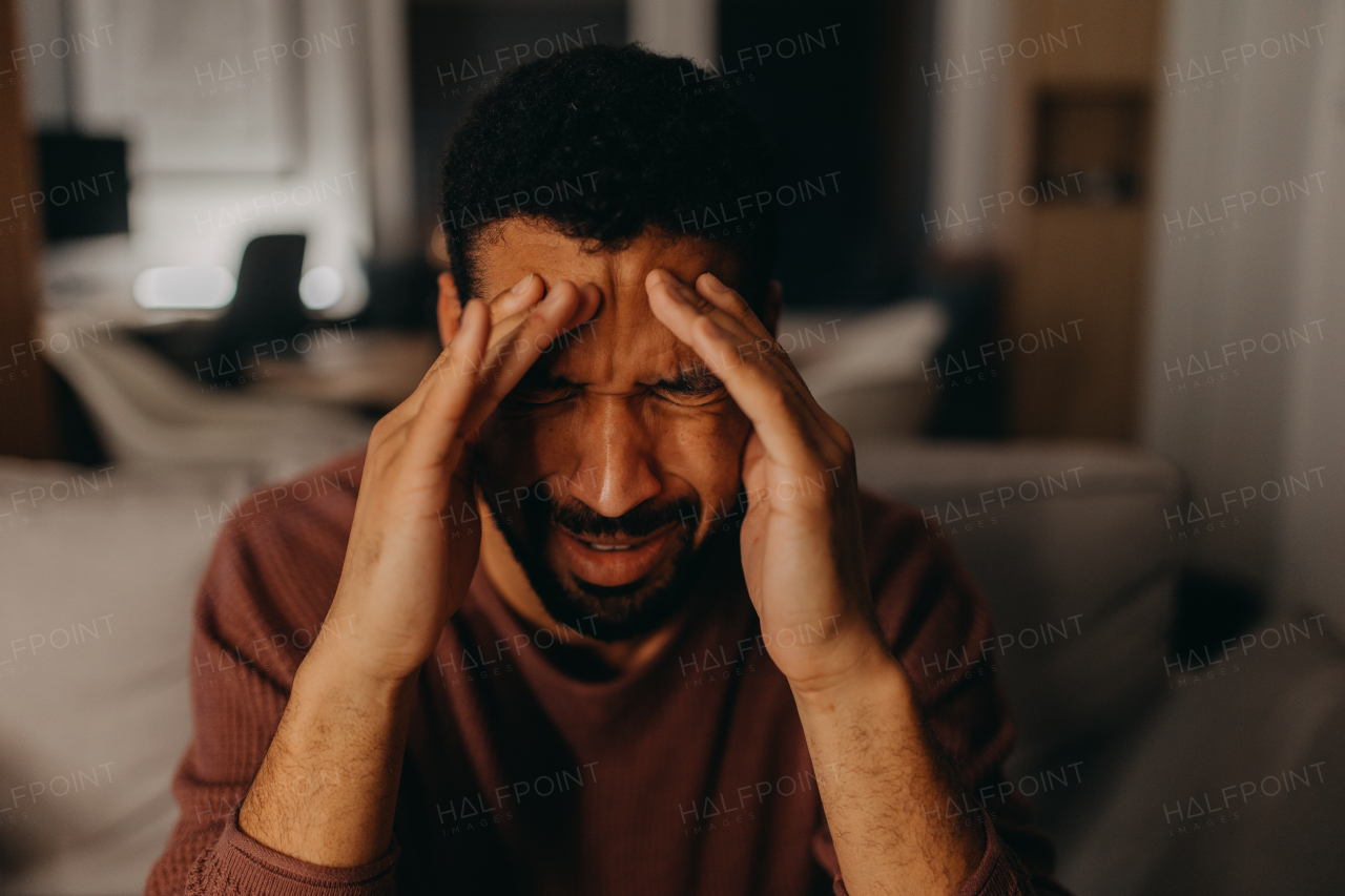 A portrait od depressed young African - American man with head in hands sitting at home.