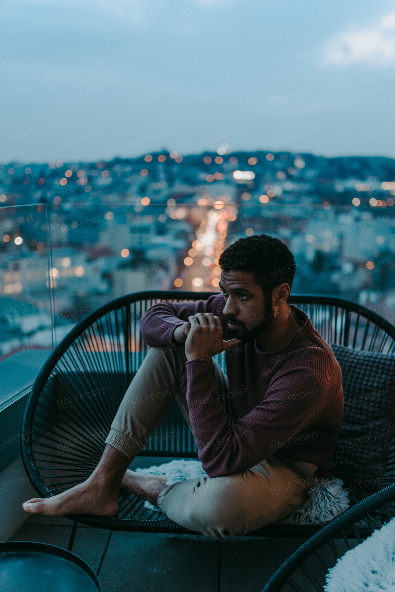 A portrait od depressed young African - American man sitting on balcony with urban view in evening.