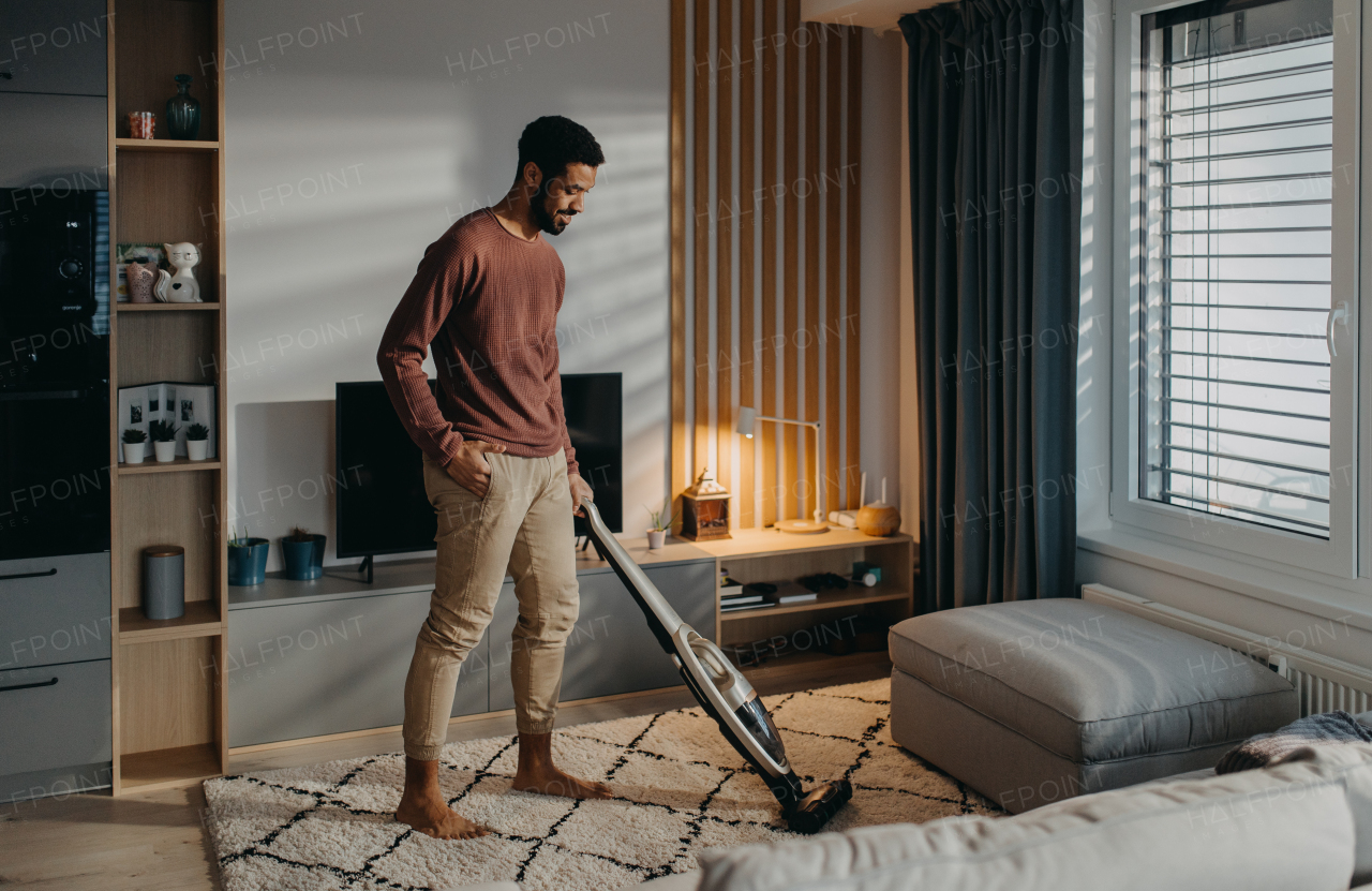 A young man hoovering carpet with vacuum cleaner in living room