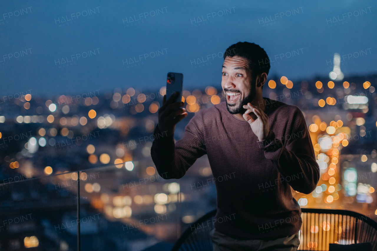 A cheerful young man taking selfie on balcony with urban view.