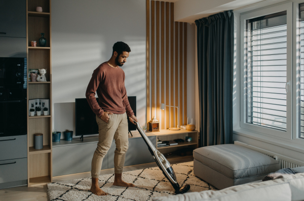 A young man hoovering carpet with vacuum cleaner in living room