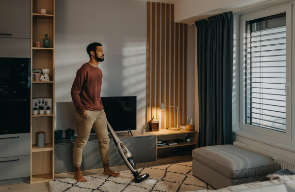 A young man vacuum cleaning carpet in living room