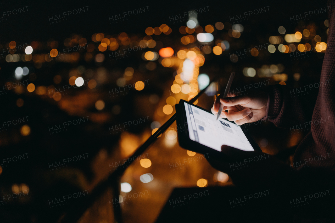 a Close-up of man standing on balcony with urban view and using tablet at night