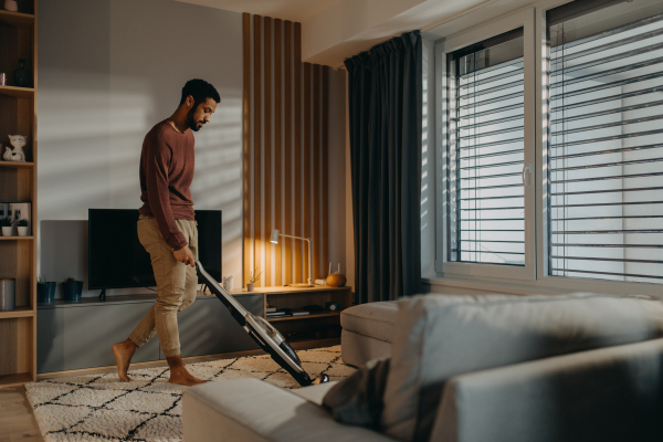 A young man vacuum cleaning carpet in living room