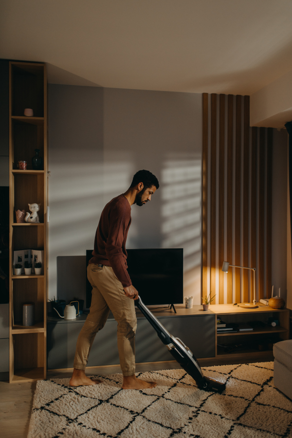 A young man vacuum cleaning carpet in living room