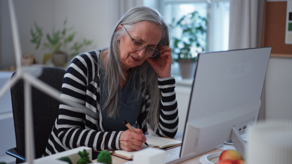 A mature business woman with working on laptop in office and having headache.