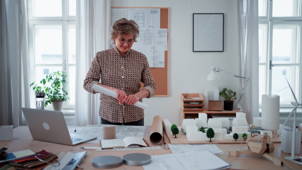 A mature woman architect putting rolled-up blueprints to tube in office.