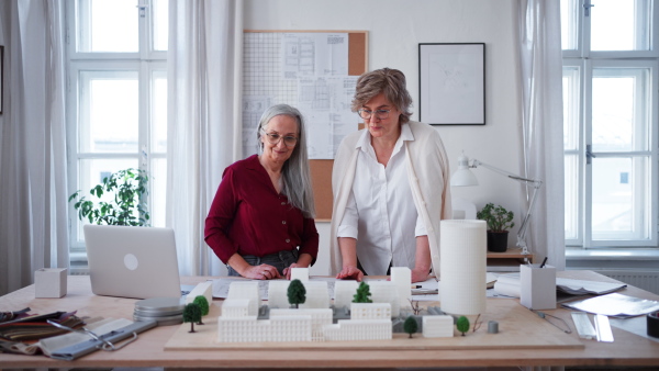 Senior women eco architects with model of modern bulidings and the blueprints working together in office.