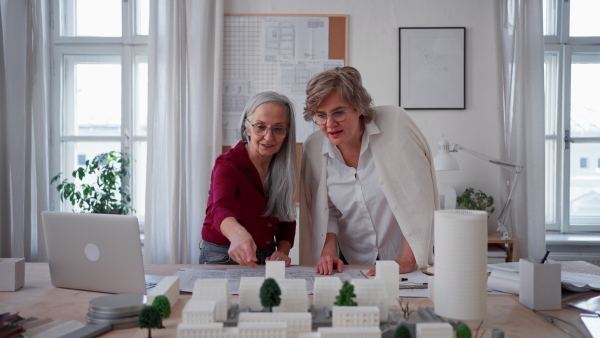 Senior women eco architects with model of modern bulidings and the blueprints working together in office.