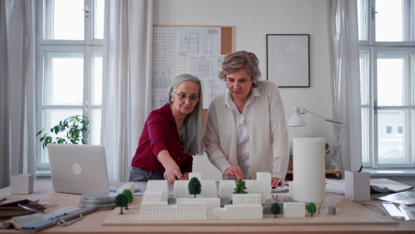 Senior women eco architects with model of modern bulidings and the blueprints working together in office.