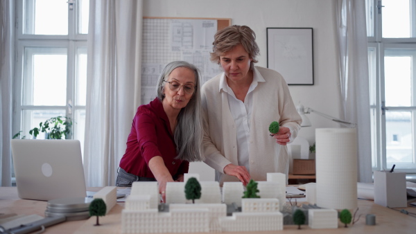 Senior women eco architects with model of modern bulidings and the blueprints working together in office.