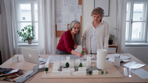 Senior women eco architects with model of modern bulidings and the blueprints working together in office.