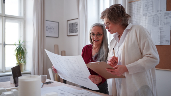 Senior women architects looking at the blueprints together in office .