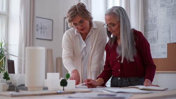 Senior women eco architects with model of modern bulidings and the blueprints working together in office.