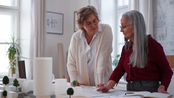 Senior women eco architects with model of modern bulidings and the blueprints working together in office.