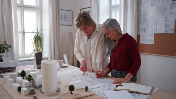 Senior women eco architects with model of modern bulidings and the blueprints working together in office.