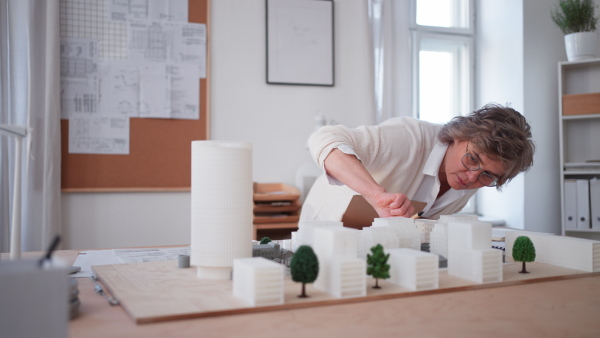 A senior woman eco architect with model of modern bulidings working in office.