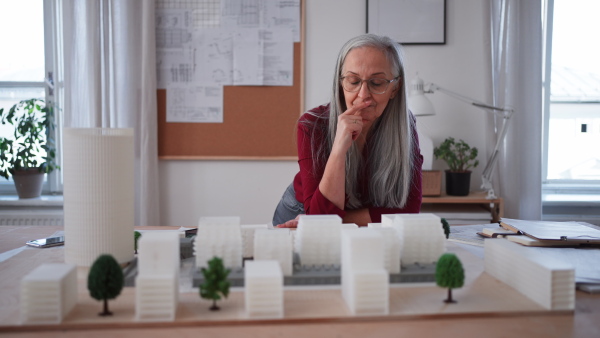 A senior woman eco architect with model of modern bulidings working in office.