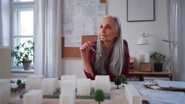 A senior woman eco architect with model of modern bulidings working in office.