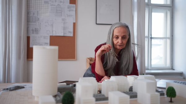 A senior woman eco architect with model of modern bulidings working in office.