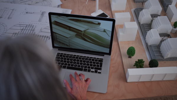 A close-up of senior woman eco architect designing modern bulding on lapotp in office.