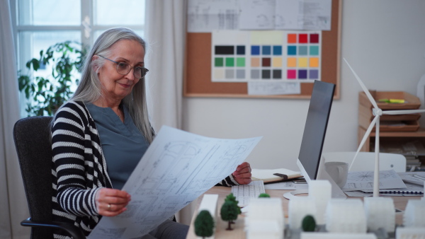 A senior woman eco architect looking at blueprints in office.