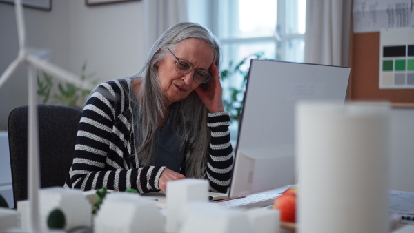 A senior woman eco architect looking at blueprints in office.