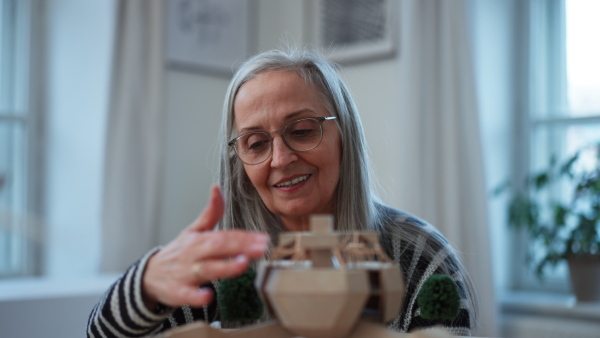 A senior woman architect holding model of modern eco buliding in office