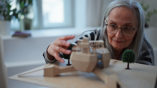 A senior woman architect holding model of modern eco buliding in office