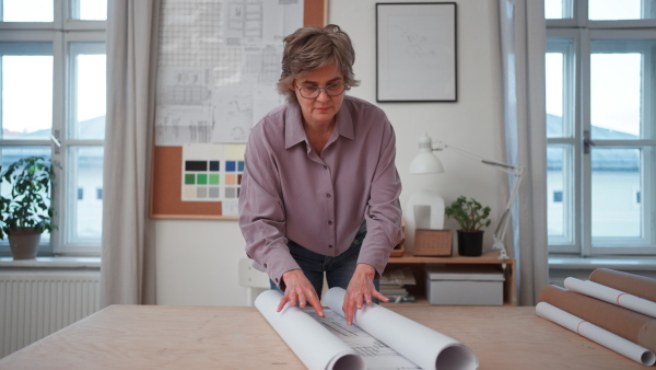 A senior woman architect with model of houses looking at blueprints in office.