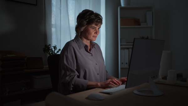 A mature business woman with working on laptop in office at night.