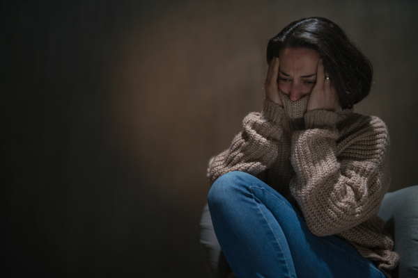 A depressed mid-adult woman sitting on the floor in the dark and crying.