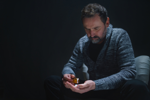 A mature man taking drug pill on dark background, mental health concept.